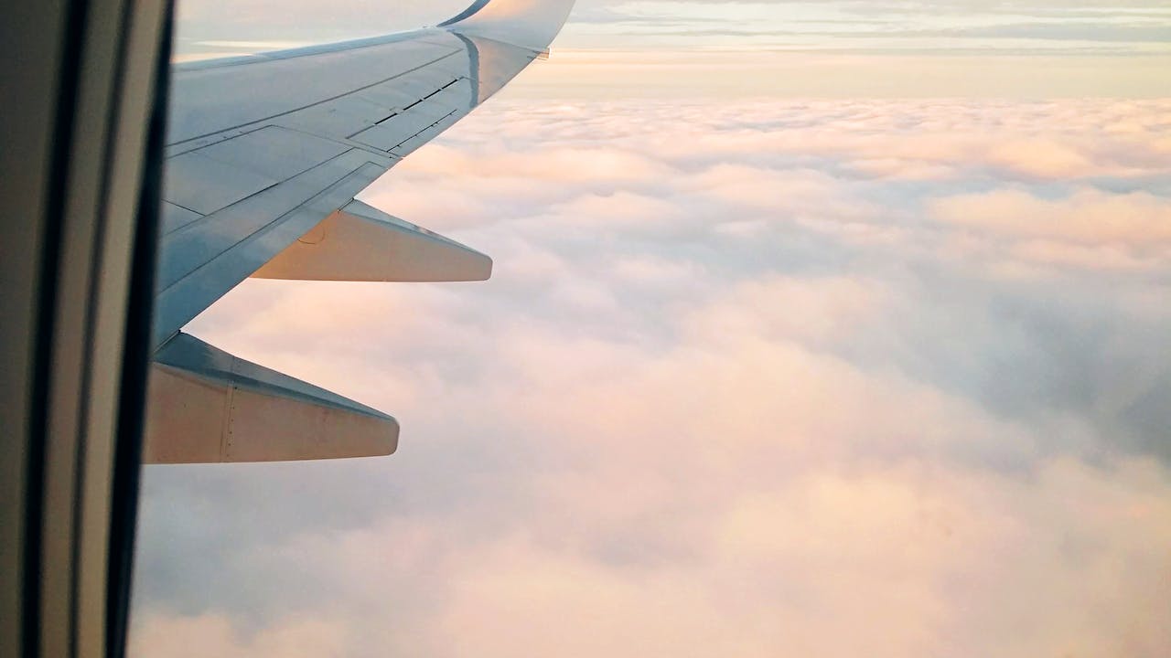 Wing of aircraft flying over clouds at sundown